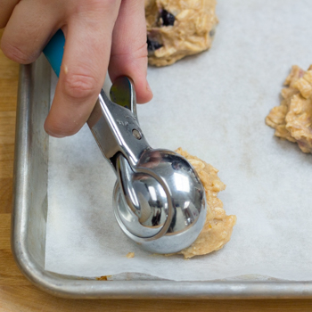 Scooping cookie dough into balls on a baking sheet.