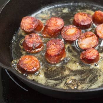 Chorizo sauteing in a cast iron pan.