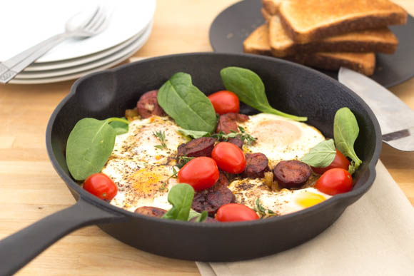 Fry-up with greens, eggs, and chorizo served in a cast iron pan.