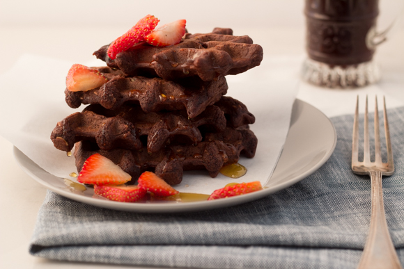 Brownie waffles on a plate, garnished with chopped strawberries.