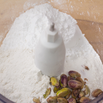 Pistachios and powdered sugar in a food processor ready to be pulsed.