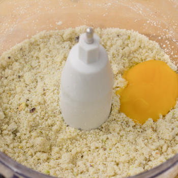Egg yolk added to ground nut mixture in food processor.
